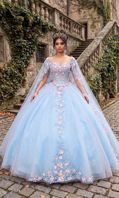 A woman stands on a cobblestone path in front of an ivy-covered stone building, wearing the Baby Blue Quinceanera Dress CHF3117 by Chicas, adorned with pink 3D floral appliques and topped with a crown.