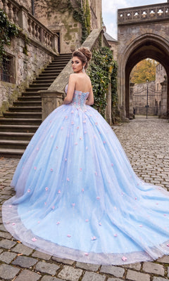 A woman wearing the Quinceanera Dress CHF3119 By Chicas, a strapless ballgown adorned with pink 3D floral appliques, stands on a cobblestone path near stone stairs and an old building.