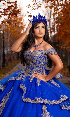 Wearing the Quinceanera Dress CHF3120 By Chicas, a woman crowned and confident poses on a leaf-covered path, surrounded by autumn trees.