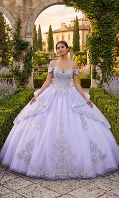 A woman wearing the Quinceanera Dress CHF3123 by Chicas in lilac and silver stands in a formal garden, surrounded by hedges, a stone arch, and a grand building in the background.