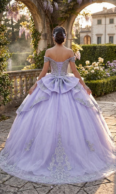 A woman wearing the Quinceanera Dress CHF3123 By Chicas, featuring lilac fabric with silver embroidery, stands outdoors on a stone path, her back to the camera, surrounded by greenery and flowers.