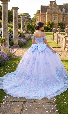 A woman wearing the Quinceanera Dress CHF3124 by Chicas, featuring a light blue off-the-shoulder design with delicate 3D floral accents, stands in a formal garden near a historic stone building, facing away from the camera.