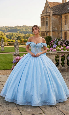 A woman in the Quinceanera Dress CHF3125 by Chicas, a baby blue off-the-shoulder glitter-tulle ballgown with a delicate corset bodice, stands on a stone patio in front of a historic mansion and colorful hydrangea bushes.