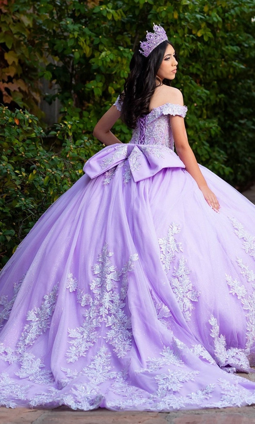 A young woman stands outdoors wearing the Quinceanera Dress CHF3128 By Chicas, a lilac gown adorned with elegant floral embroidery and a large bow, complemented by a matching crown.