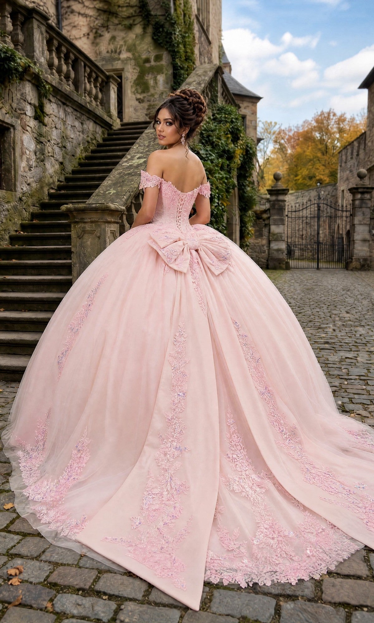 A woman wearing the Quinceanera Dress CHF3130 By Chicas, featuring an ornate off-the-shoulder design with a corset-style bodice and a flowing tulle ballgown skirt, stands on a cobblestone path near stone stairs, glancing over her shoulder.