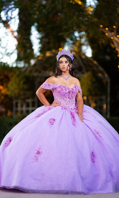 A young woman wearing the Quinceanera Dress CHF3133 By Chicas—a sparkling lavender glitter tulle ballgown with a corset bodice and a tiara—stands outdoors with greenery in the background.
