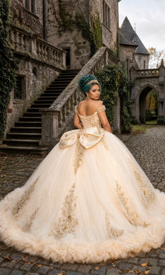 Wearing the Quinceanera Dress CHF3135 By Chicas, a woman stands on a cobblestone path in front of an ivy-clad stone building. The gown’s gold embellishments, lace-up back, large bow, and off-the-shoulder design create a look of timeless elegance.