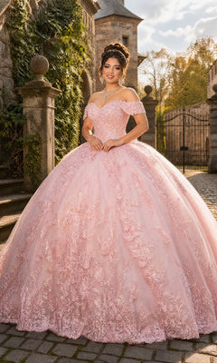 A young woman in the Quinceanera Dress CHF3138 By Chicas, a blush off-the-shoulder tulle ballgown, stands outdoors among stone architecture and greenery, smiling at the camera.