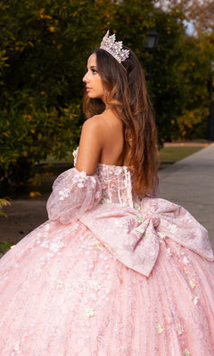 A young woman stands outdoors in the Quinceanera Dress CHF3140 By Chicas—a pastel ballgown adorned with delicate 3D floral appliques and paired with a jeweled crown—looking elegantly to the side.