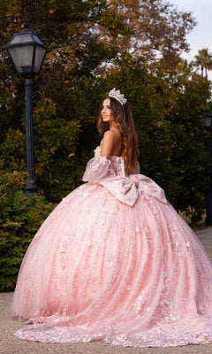 Wearing the Quinceanera Dress CHF3140 by Chicas, a woman stands outdoors in a voluminous pastel ballgown adorned with delicate 3D floral appliques, glancing back over her shoulder as her tiara sparkles in the light.