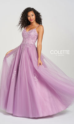 A woman poses against a plain background in the Long Prom Dress CL12212 by Colette—a floor-length lavender tulle ball gown featuring lace, floral embroidery, and thin straps for an elegant touch.