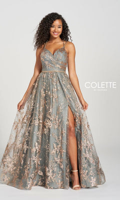 A woman poses against a plain background in the Gold and Pewter Prom Ball Gown Colette CL12218, featuring a sleeveless design, long A-line silhouette, floral lace overlay, fitted bodice, and a thigh-high slit.