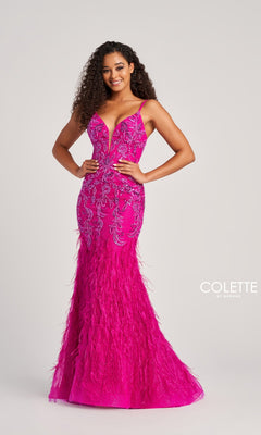 A woman stands with hands on hips against a plain background, wearing the Long Colette CL5103 Feathered Mermaid Prom Dress featuring bright pink feathers, intricate beadwork, and a floor-length skirt.