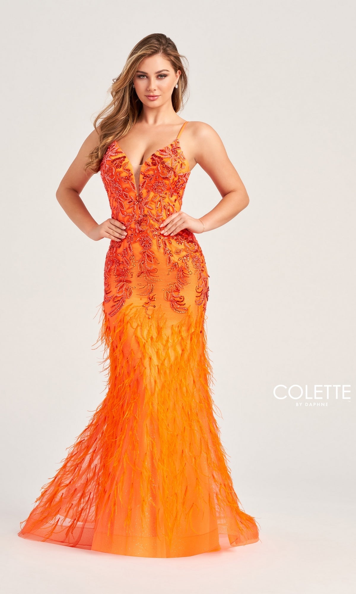A woman models the Long Colette CL5103 Feathered Mermaid Prom Dress, featuring a fitted bright orange design with feathers, embroidered detailing, a deep V neckline, and thin straps for an elegant formal look.
