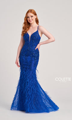 A woman with long red hair wears the Long Colette CL5103 Feathered Mermaid Prom Dress in royal blue, featuring beaded details, as she stands against a plain light background.