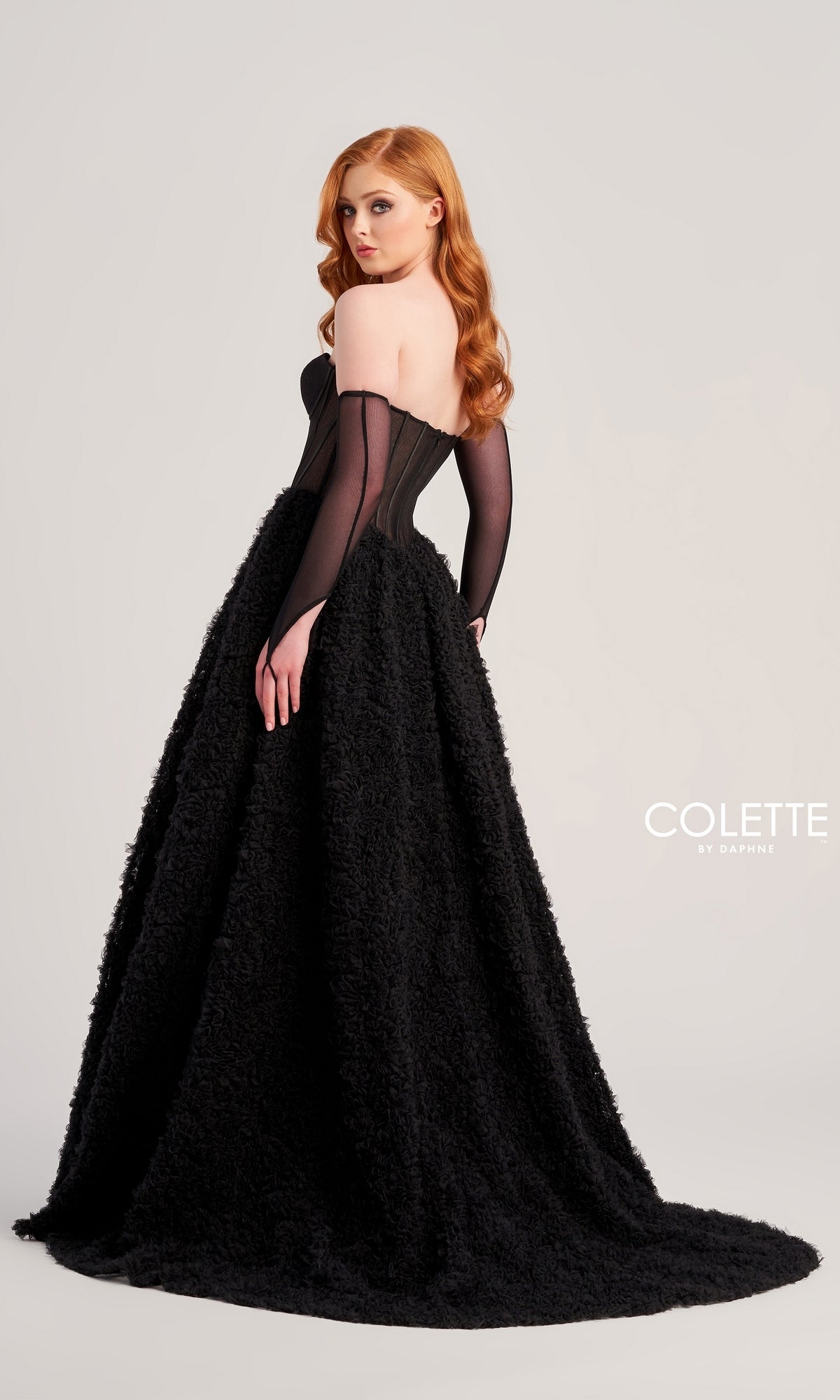 A woman with long red hair models the Bustier Colette Long A-Line Prom Ball Gown CL5114, which has an off-shoulder black top and a textured, floor-length skirt, against a plain light background. 
