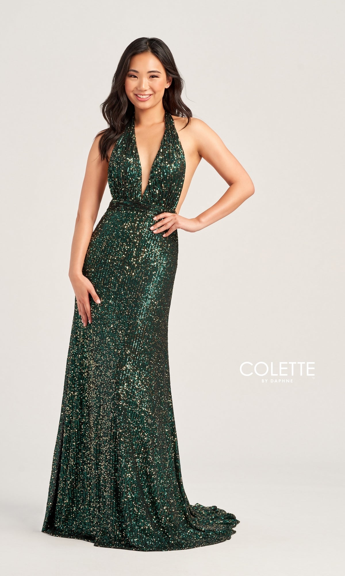 A woman smiles against a plain light background, wearing the Colette Long Sequin Halter Prom Dress CL5115—a sleeveless, deep V-neck, floor-length dark green sequin gown. The 