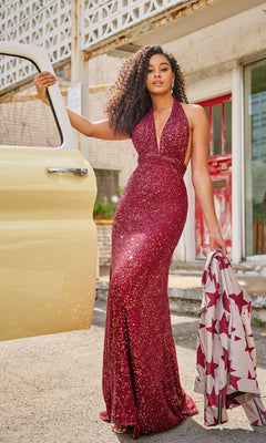 A woman in a Colette Long Sequin Halter Prom Dress CL5115 stands by an open car door, holding a star-patterned jacket, with a building in the background.