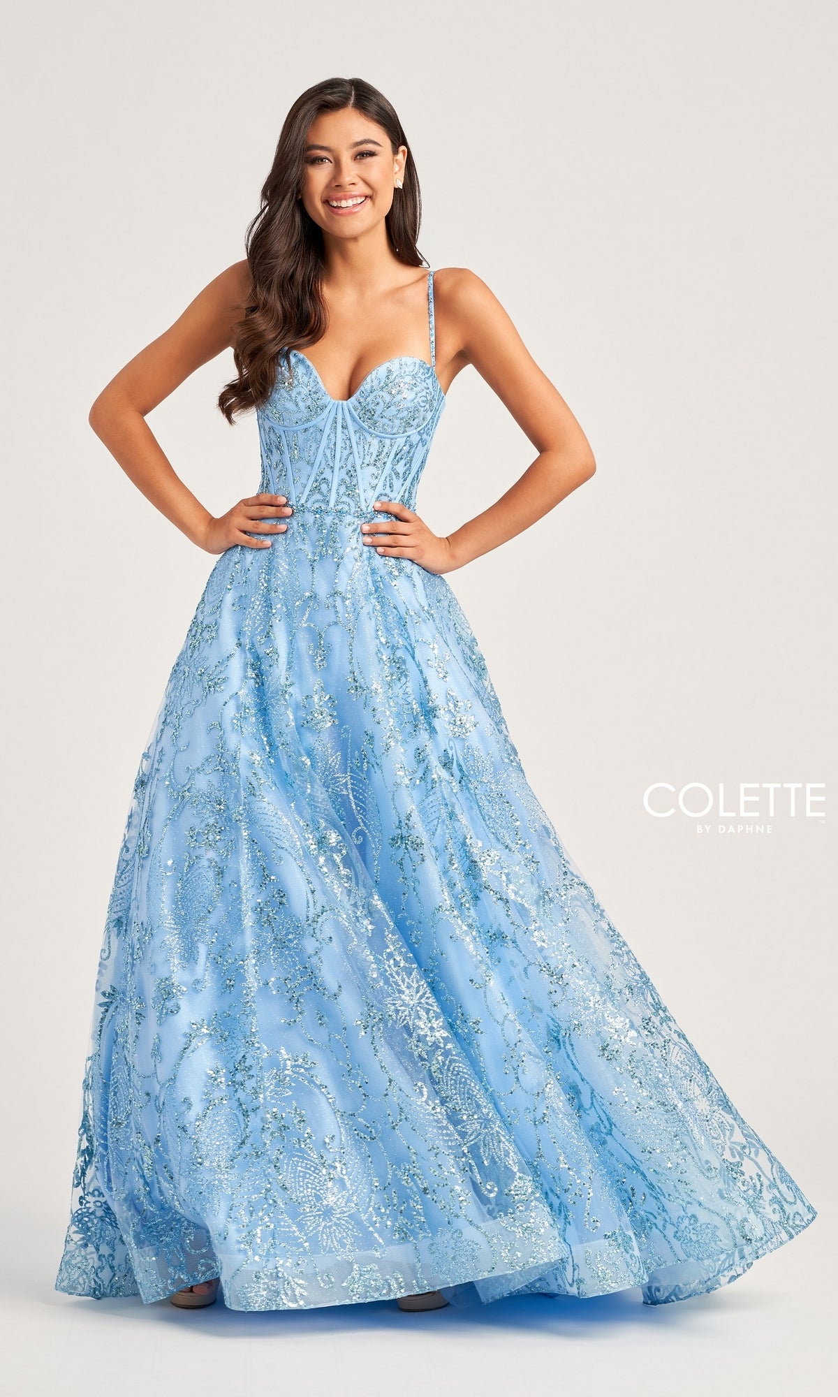 A woman smiles against a light background in the Colette Glitter-Tulle Long Prom Ball Gown CL5117—a light blue, floor-length A-line dress with sparkling floral embroidery and a corset-style open back.