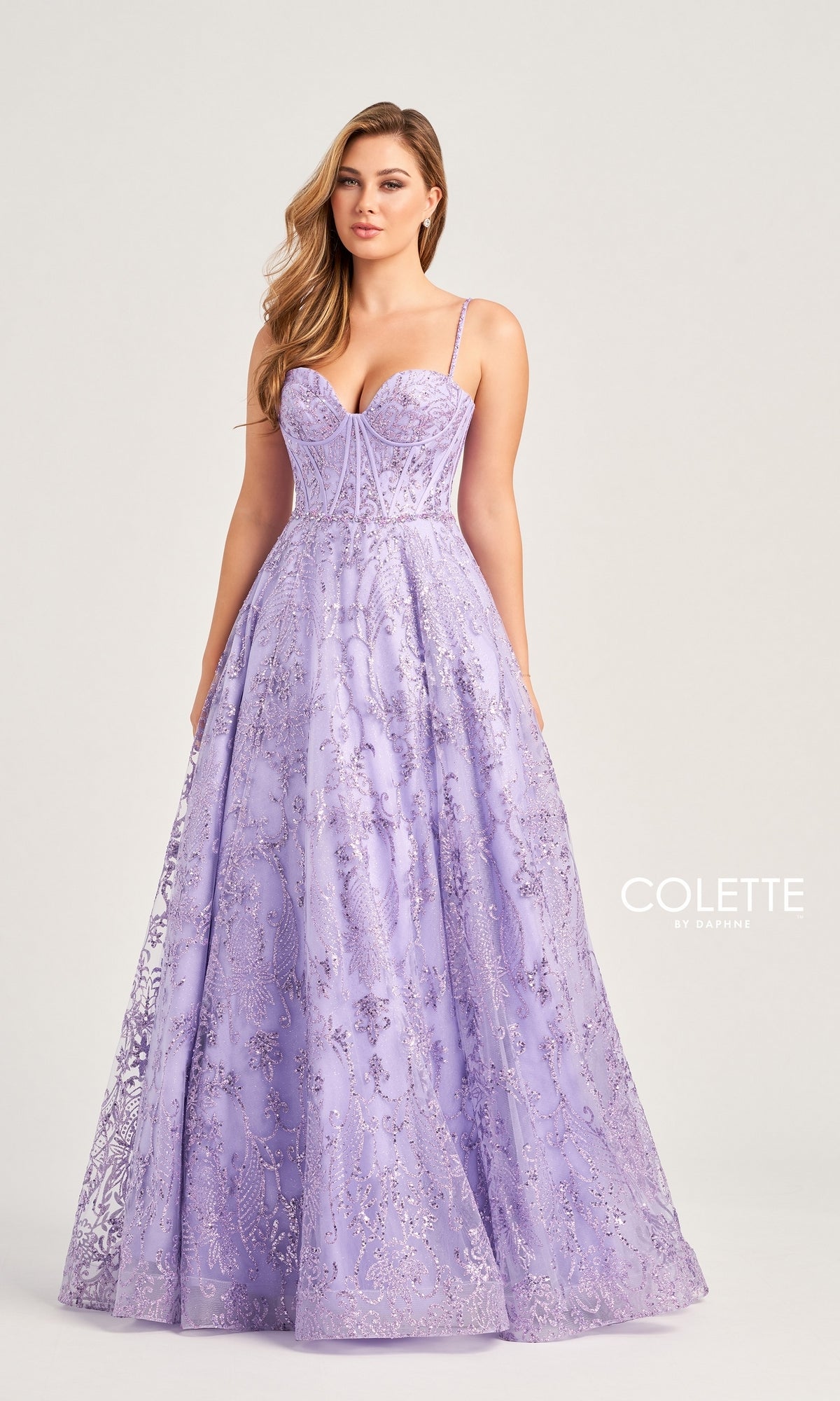 A woman in the Colette Glitter-Tulle Long Prom Ball Gown CL5117, featuring a lavender hue, thin straps, intricate beading, and a full skirt, stands against a plain background. 