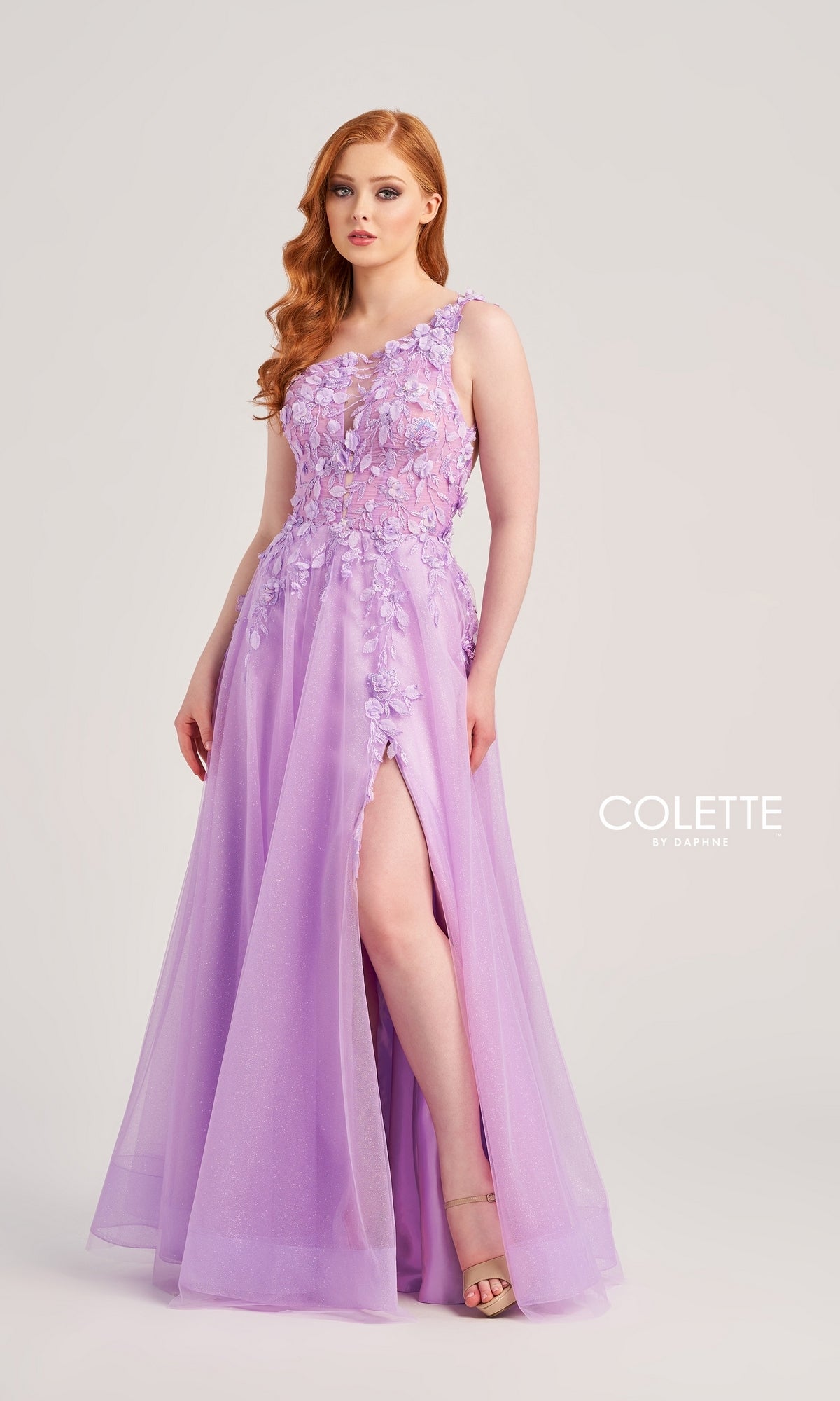 A woman wears the Colette One-Shoulder Designer Prom Dress CL5124 with floral embroidery and a thigh-high slit, standing against a neutral background. 