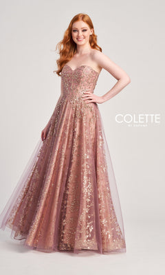 A woman in the Colette Strapless Sweetheart Prom Ball Gown CL5144—floor-length blush pink with gold embellishments—stands smiling against a plain background, one hand on her hip. The text "COLETTE BY DAPHNE" appears beside her.