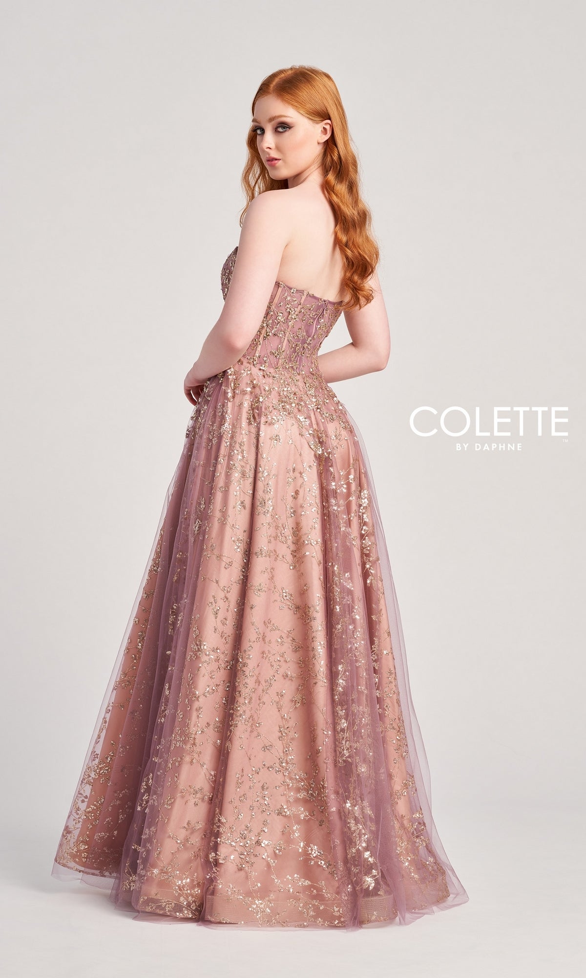 A woman with long red hair poses in the Colette Strapless Sweetheart Prom Ball Gown CL5144—floor-length mauve with gold floral accents—against a plain background. The 