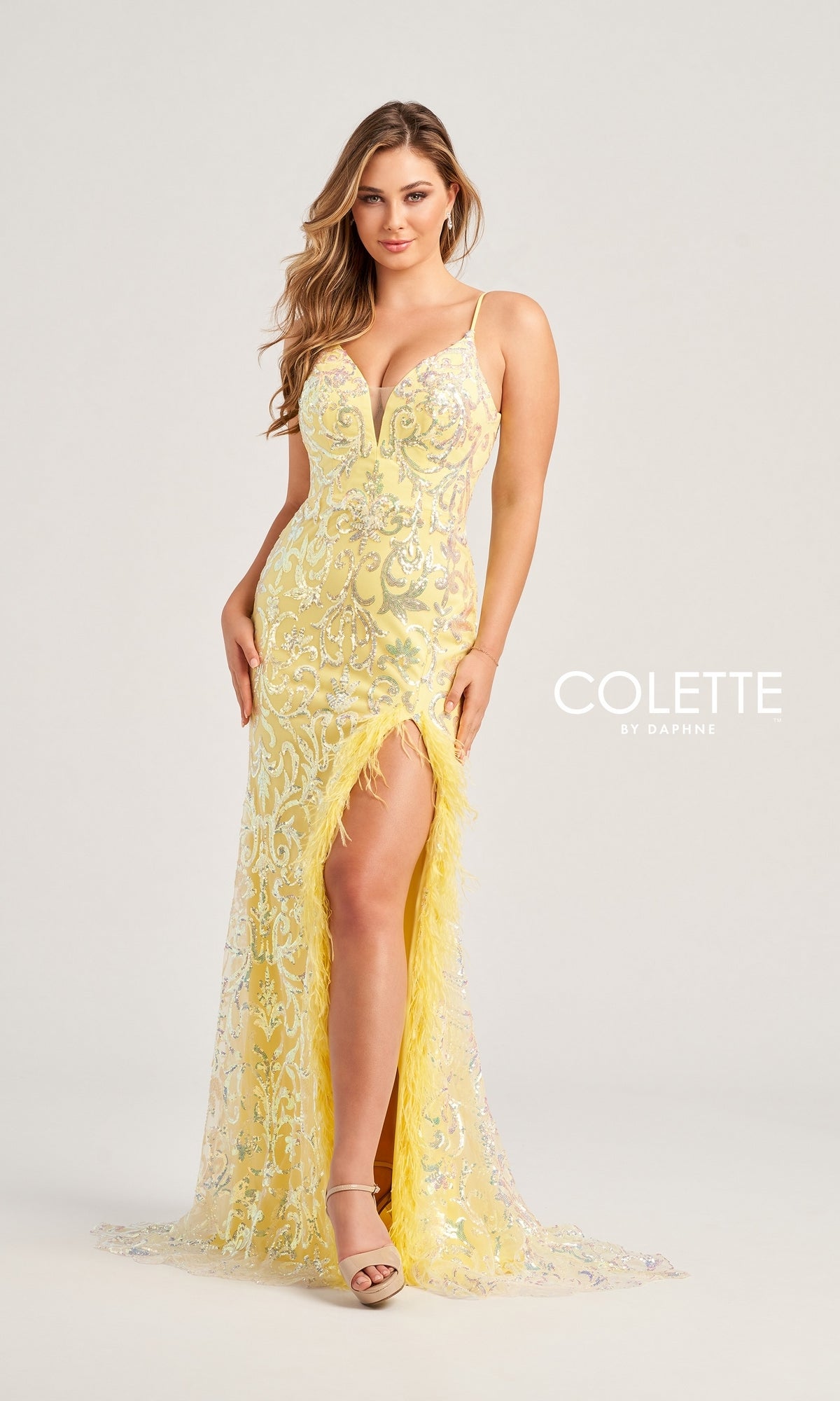 A woman poses in the Feather-Sequin Colette Long Prom Dress CL5155, a floor-length yellow gown featuring a deep V neckline, spaghetti straps, sequin detailing, and a thigh-high slit against a plain light background.