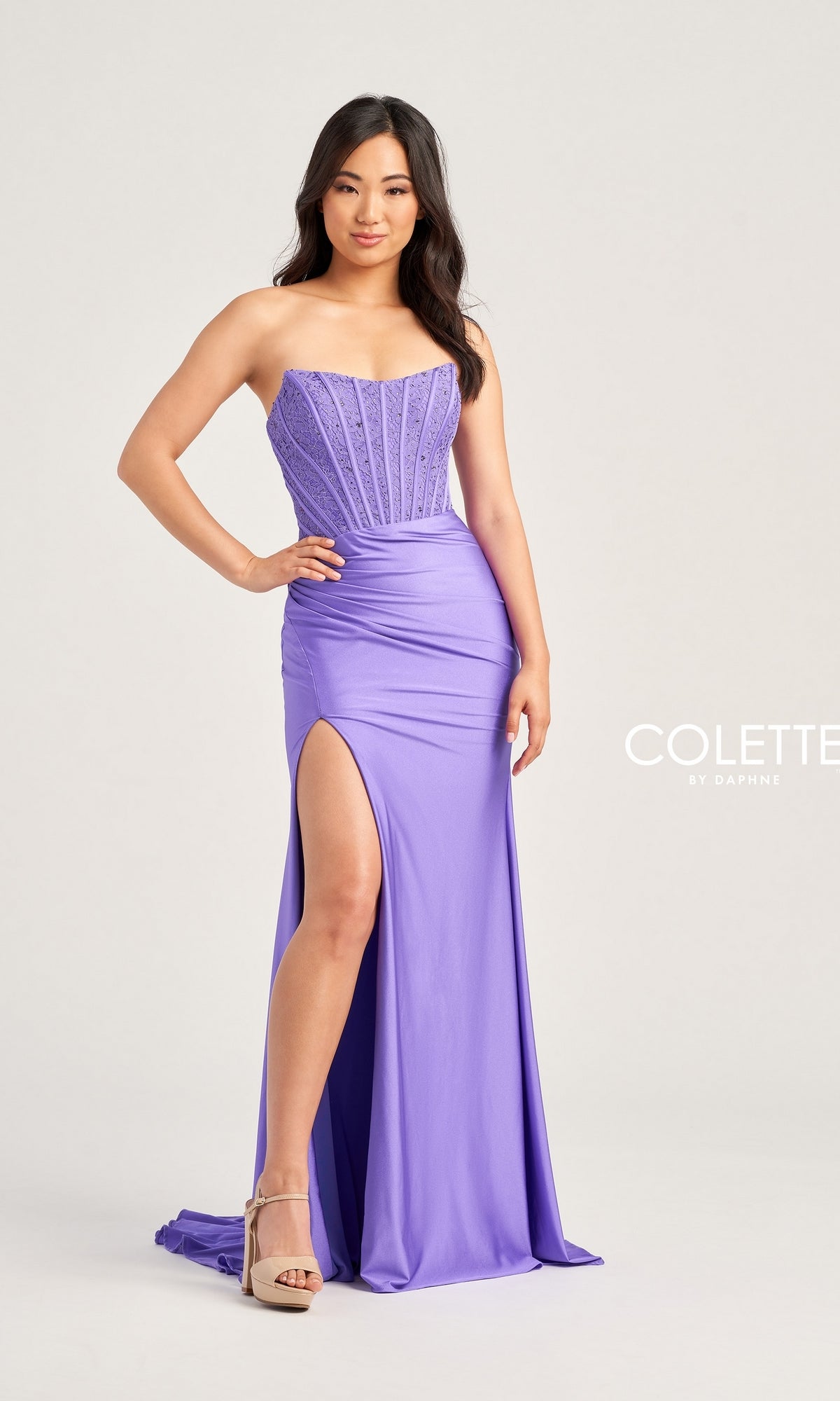 A woman models the Strapless Colette Long Designer Prom Dress CL5158, featuring a beaded corset bodice and thigh-high slit, with nude heels, against a plain light background.