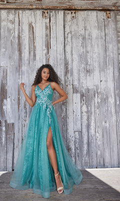 A woman poses in front of a weathered wooden wall wearing the Glitter-Lace Colette Long Prom Ball Gown CL5197, a turquoise sleeveless a-line dress with beaded-lace floral applique and a high slit.