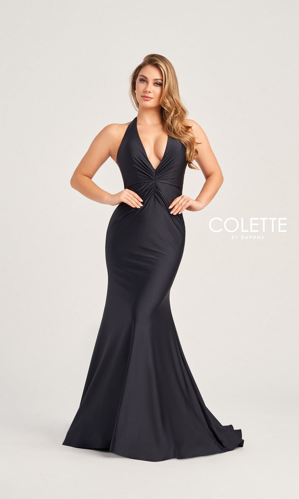 A woman poses against a plain light background in the Colette Front-Knot Long Halter Prom Dress CL5199, a sleeveless, floor-length black gown made of stretch spandex jersey with a deep V-neckline. 
