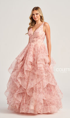 A woman wears the Colette Tiered Long Print Prom Ball Gown CL5273, a sleeveless pink floral dress with a deep V-neckline and layered ruffles, standing against a plain light background.