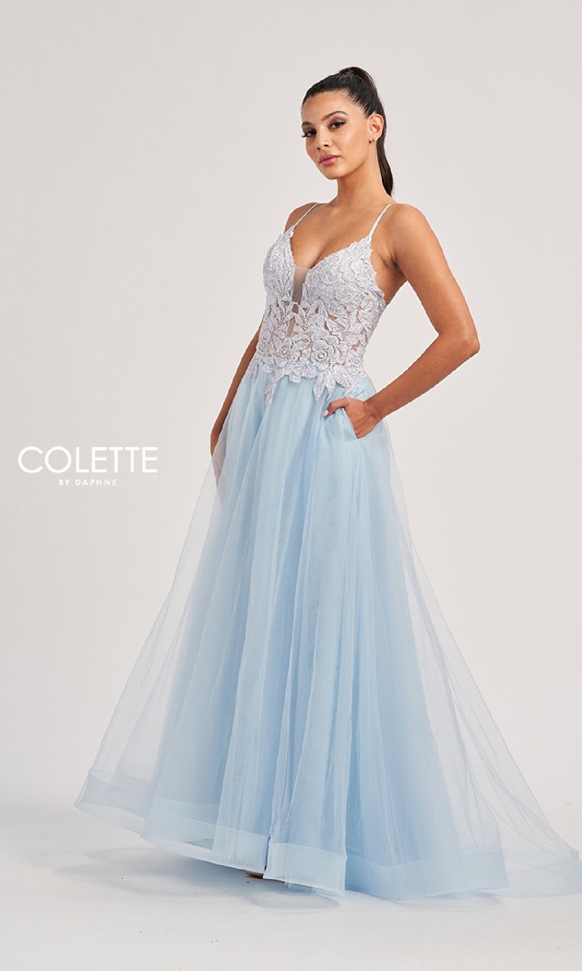 A woman wearing the Long Prom Dress: Colette CL8100—a pastel blue A-line gown with a tulle skirt, white lace embroidery bodice, and thin straps—stands against a plain background.