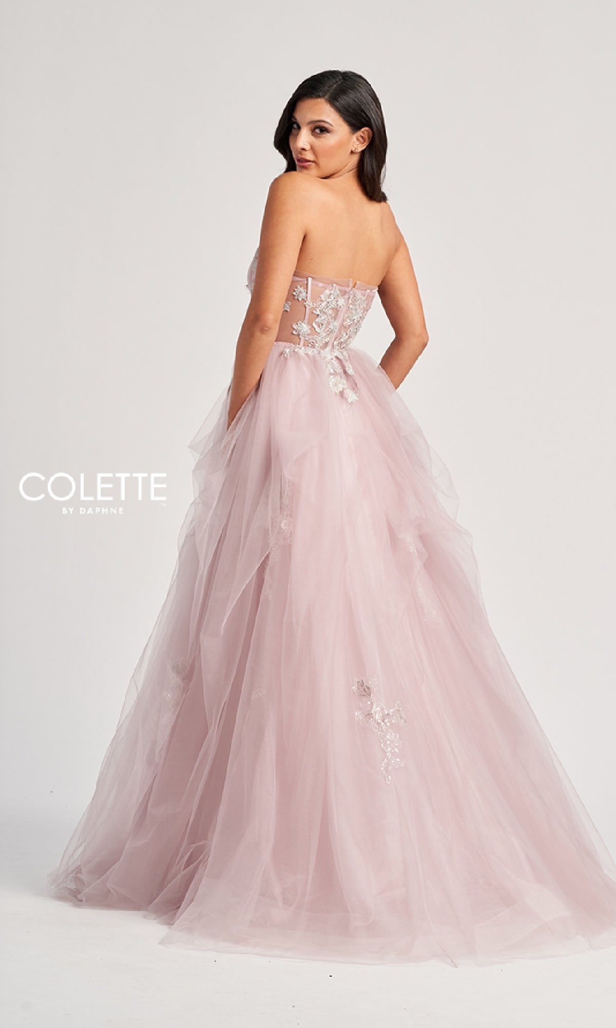 A woman models the Colette CL8120 long prom dress featuring a strapless, fitted bodice, blush pink tulle A-line skirt, and floral embellishments, posed against a plain white background.