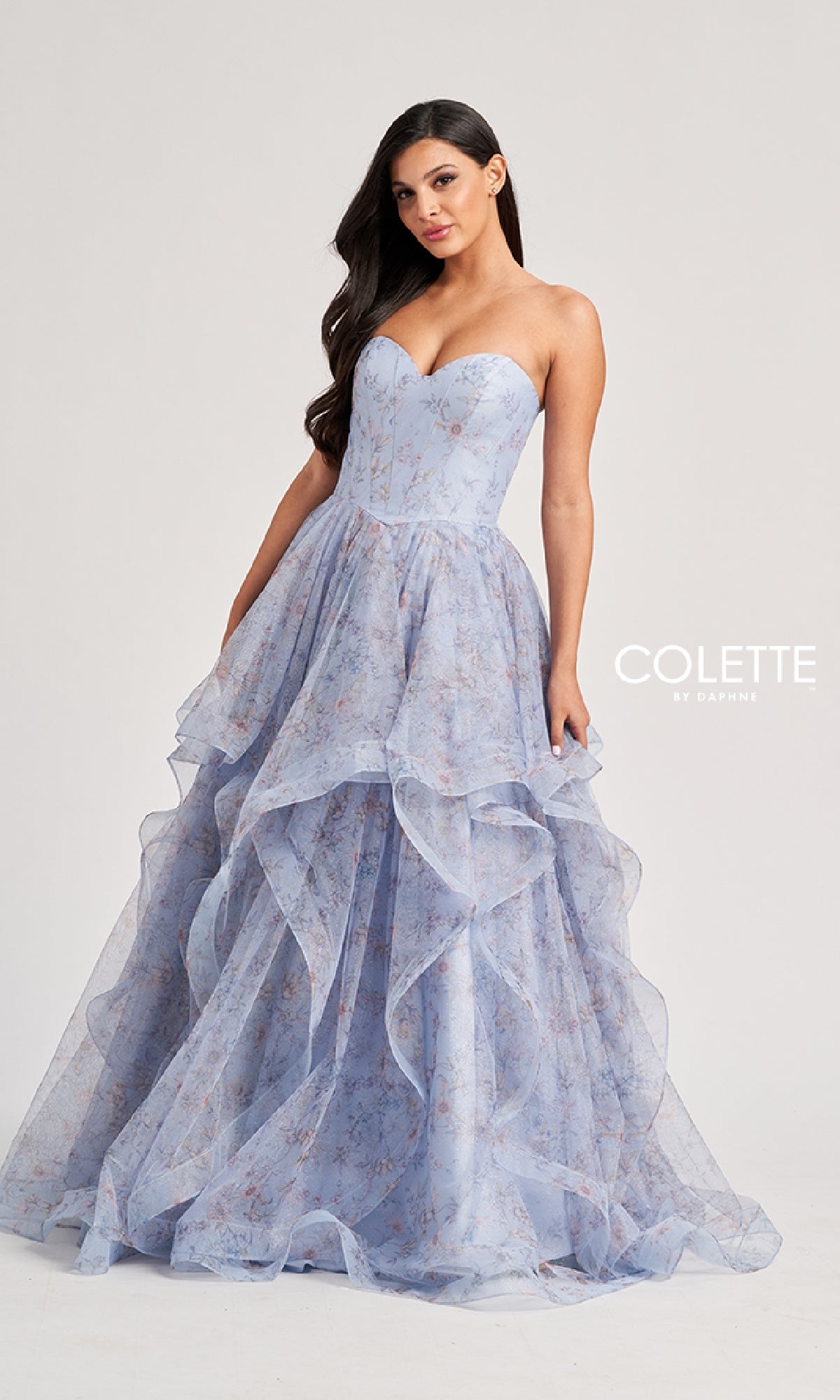 A woman wears the Colette by Daphne Long Prom Dress CL8180—a light blue, strapless ball gown with a sweetheart neckline and layered tulle skirt featuring floral patterns. The text 