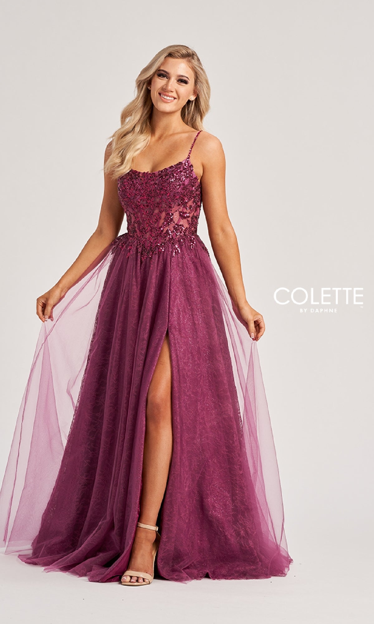 A woman stands against a plain background wearing the Colette CL8240, a sleeveless, floor-length mauve prom dress featuring an embroidered bodice, tulle overlay, floral embellishments, and a high slit.