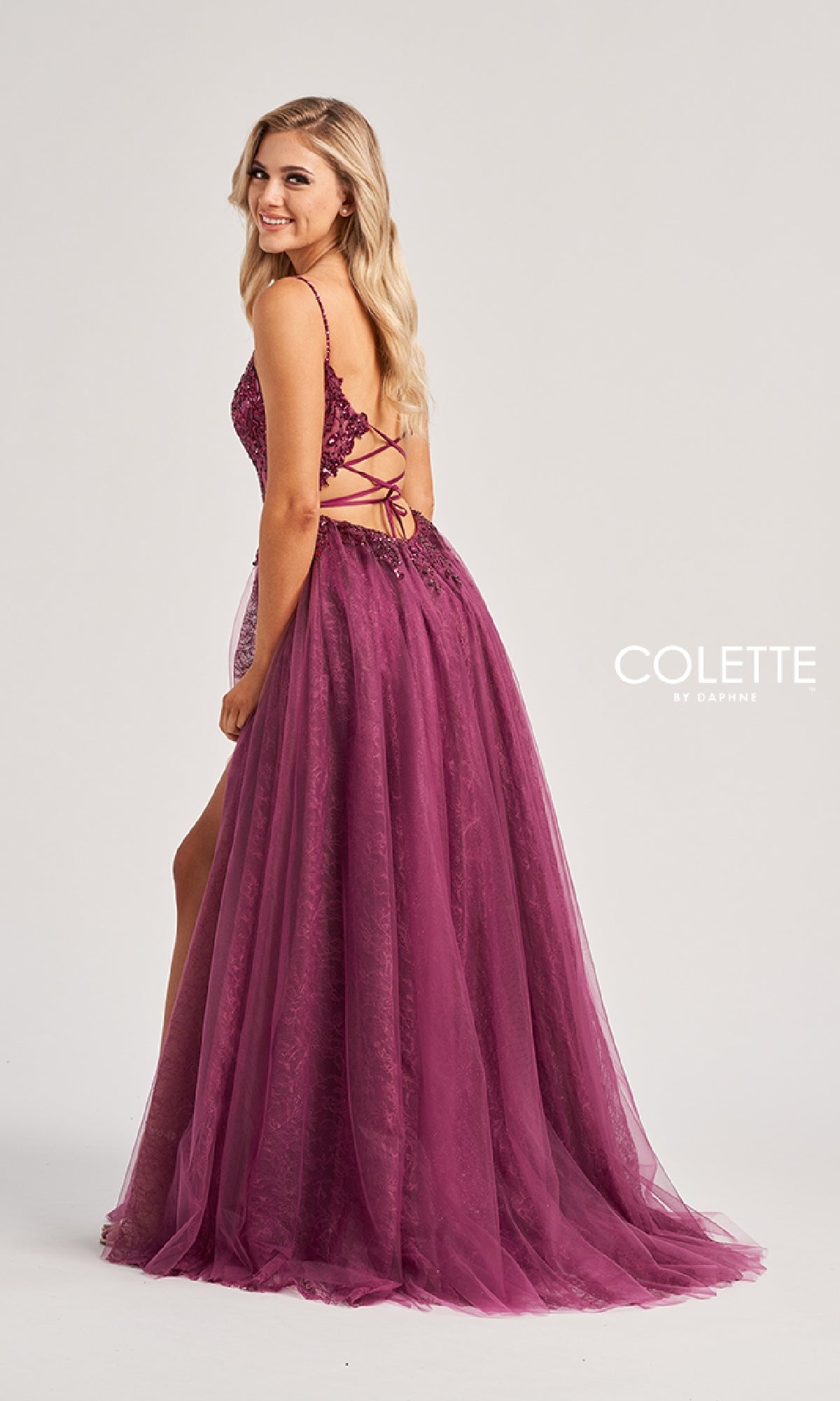 A woman models the magenta Colette CL8240 Long Prom Dress, featuring an A-line skirt, embroidered bodice, and lace-up back, standing sideways against a plain background. The 