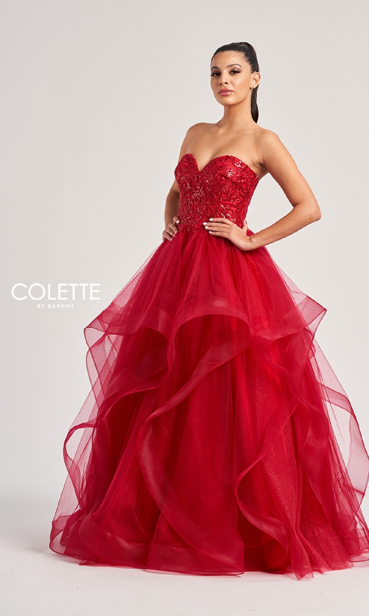 A woman poses in the vibrant red Colette CL8290 long prom dress, featuring a strapless sequined bodice and layered tulle A-line skirt. 