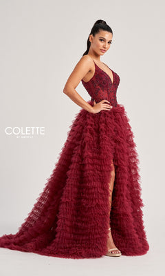 A woman in the Colette CL8330 long prom dress, featuring a sleeveless deep red design with a tiered ruffled skirt and high slit, stands against a plain light background. Text: "COLETTE by Daphne.