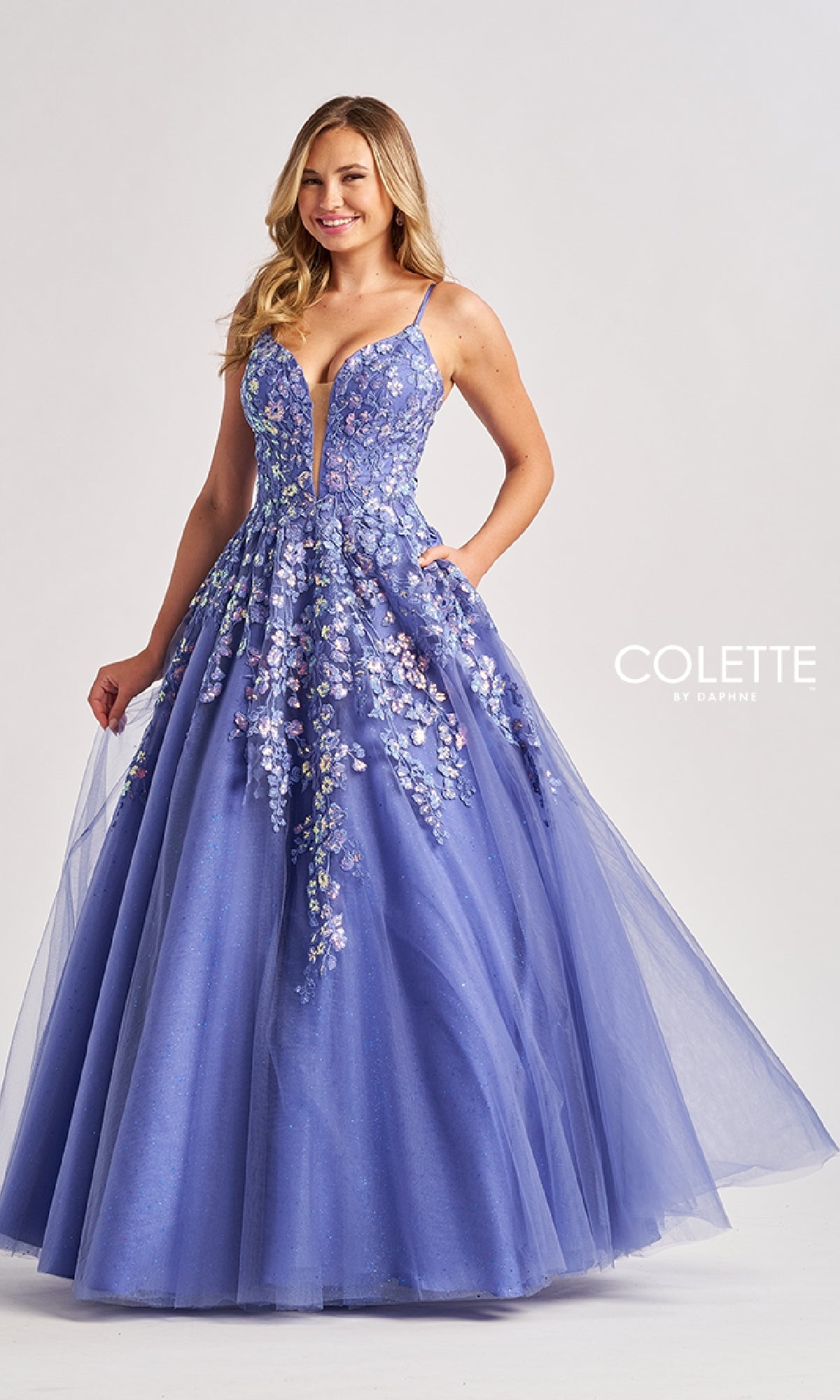 A woman stands against a plain background wearing the Colette CL8420, a sleeveless, floor-length lavender prom ball gown featuring glitter details and a low V-neckline.