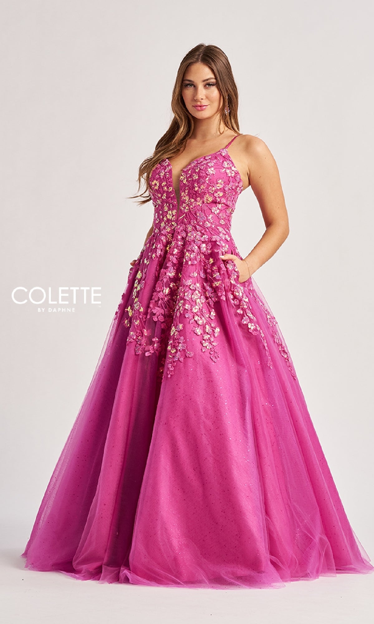 A woman poses against a light background in the Colette CL8420 Low V-Neck Glitter Prom Ball Gown, a floor-length designer dress with a fitted bodice and thin straps, exuding elegance.