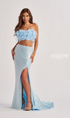 A woman stands against a plain background with the "Colette by Daphne" logo, wearing the Colette CL8450 long prom dress featuring a light blue feathered crop top and sequined floor-length skirt.