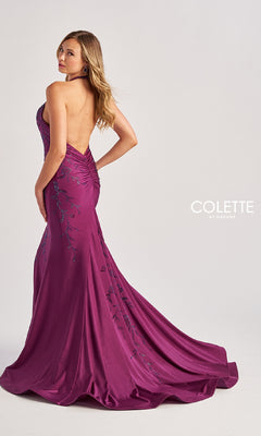 A woman poses in a floor-length magenta mermaid prom dress with beaded floral patterns and a ruched back, branded as Colette CL8455 (Long Halter Prom Dress), against a plain background.