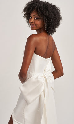 Model wears the Colette CL8470 Back Bow Strapless Long Prom Dress, posing and smiling over her shoulder to showcase the statement bow against a plain background.