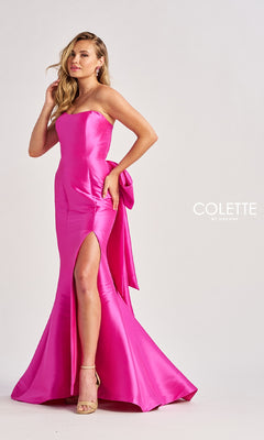 A woman stands against a plain background wearing the Colette CL8470 Back Bow Strapless Long Prom Dress in bright pink satin with a thigh-high slit, back bow detail, and beige high-heeled sandals.