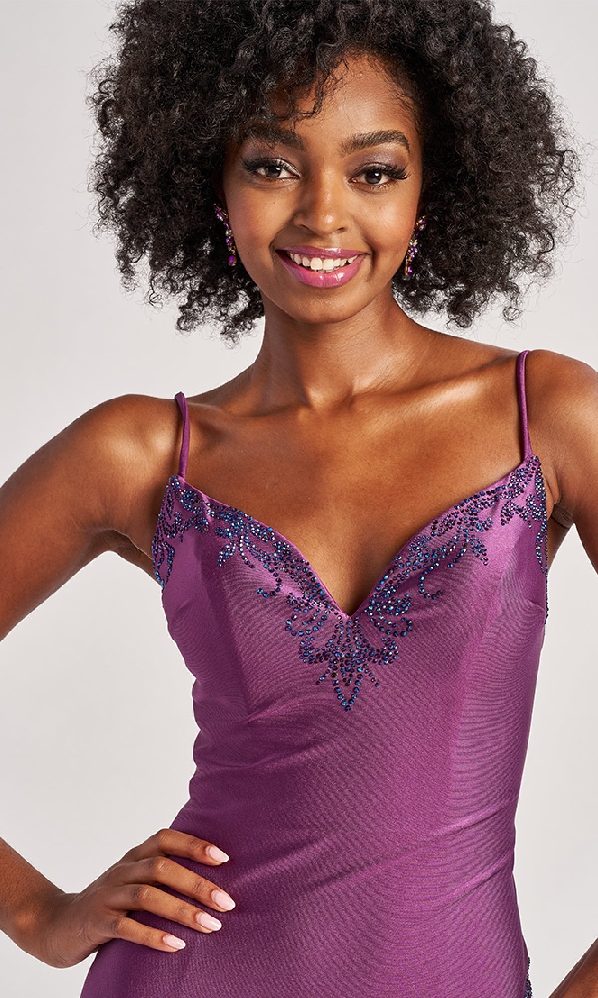 Smiling woman poses with one hand on her hip, wearing the Colette CL8485 long prom dress—a sleeveless purple bodycon gown with shimmering beaded detailing.
