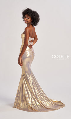 A woman wears the Colette CL8545 long prom dress in gold metallic, featuring a fitted floor-length silhouette and an open crisscross back, standing against a plain background.