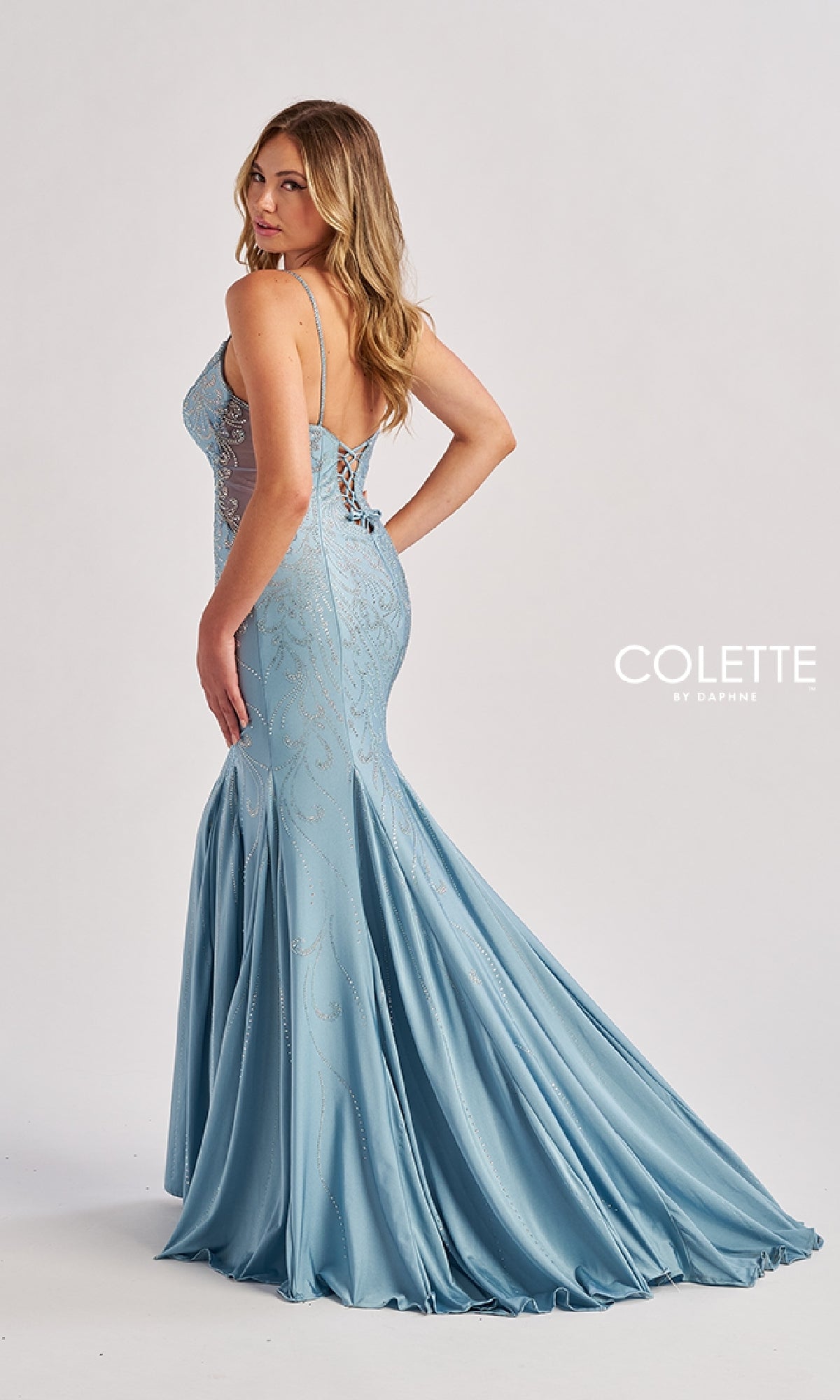 A woman in the Long Prom Dress: Colette CL8550, a light blue, floor-length fitted mermaid gown with thin straps and a lace-up back, stands against a plain light background.