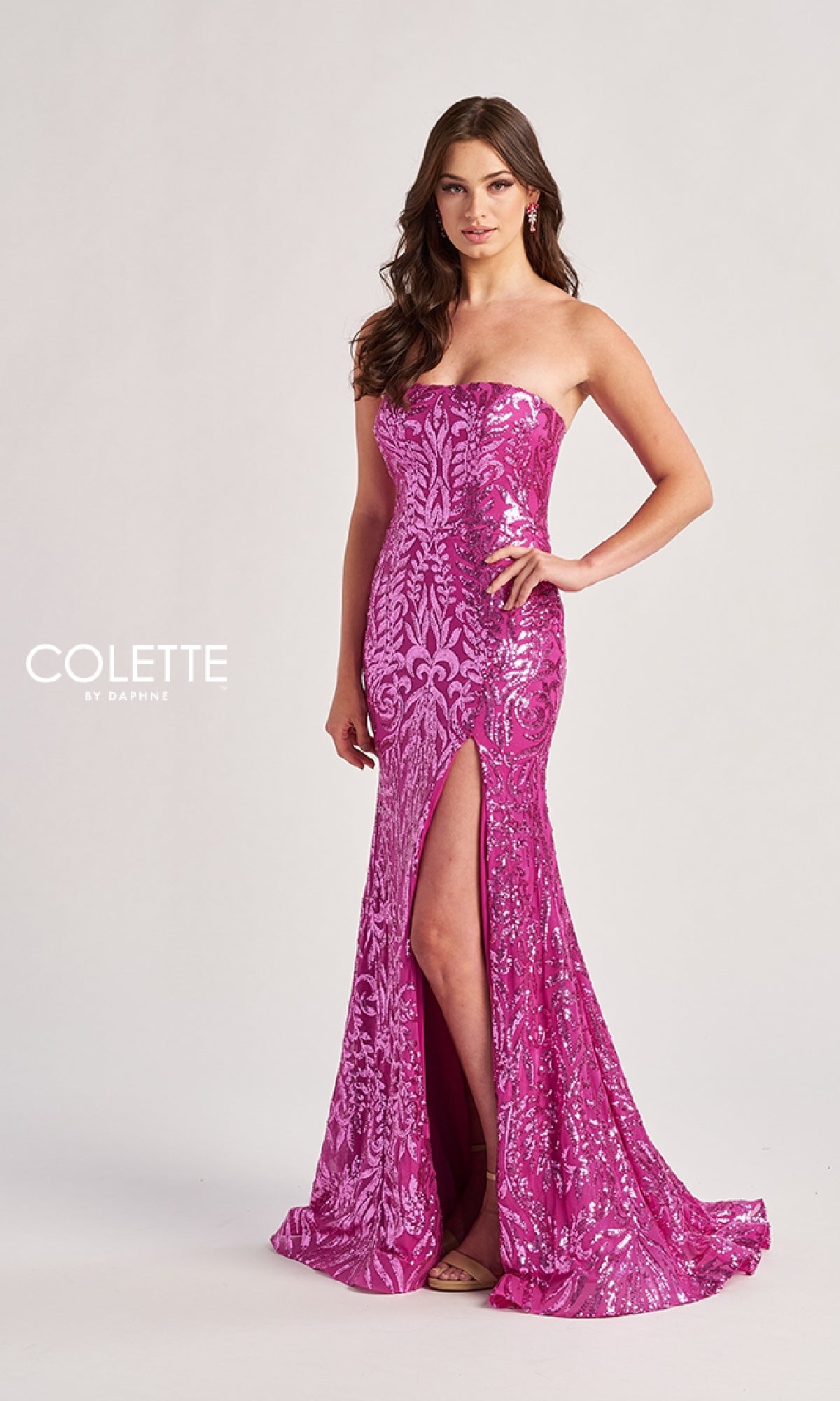 A woman in the Colette CL8610 long prom dress, featuring a strapless sequined design and a thigh-high slit, stands against a light background, her elegant gown shimmering as it catches the light.