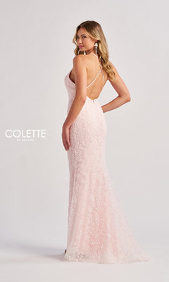 A woman stands in a studio wearing the Colette CL8655, a light pink, floor-length lace prom dress with a v-neckline and thin crisscross back straps, set against a plain background.